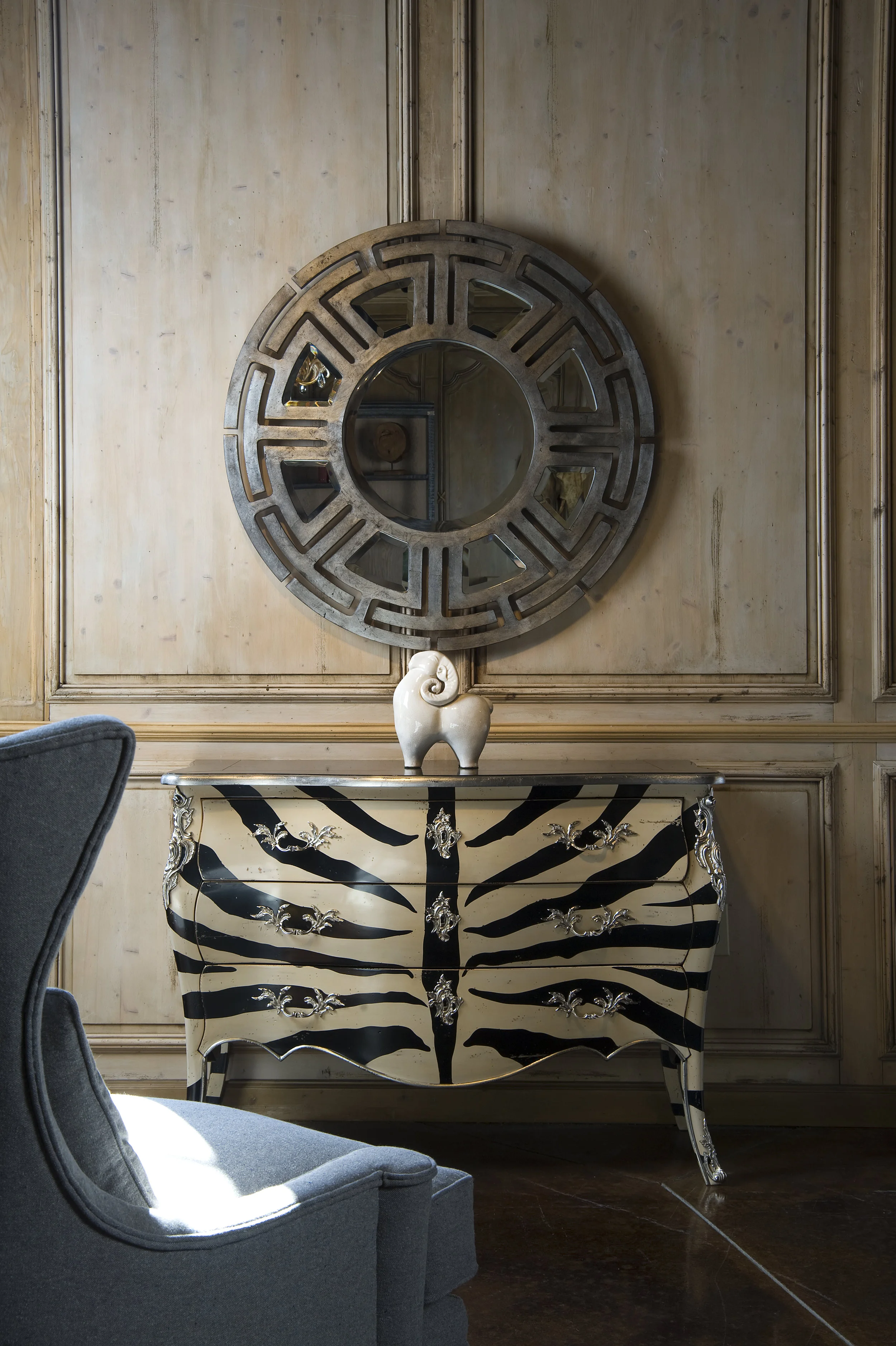 Ink illustration of a decorative bombe chest under a round mirror with a small ceramic figurine, drawn in muted earthy tones