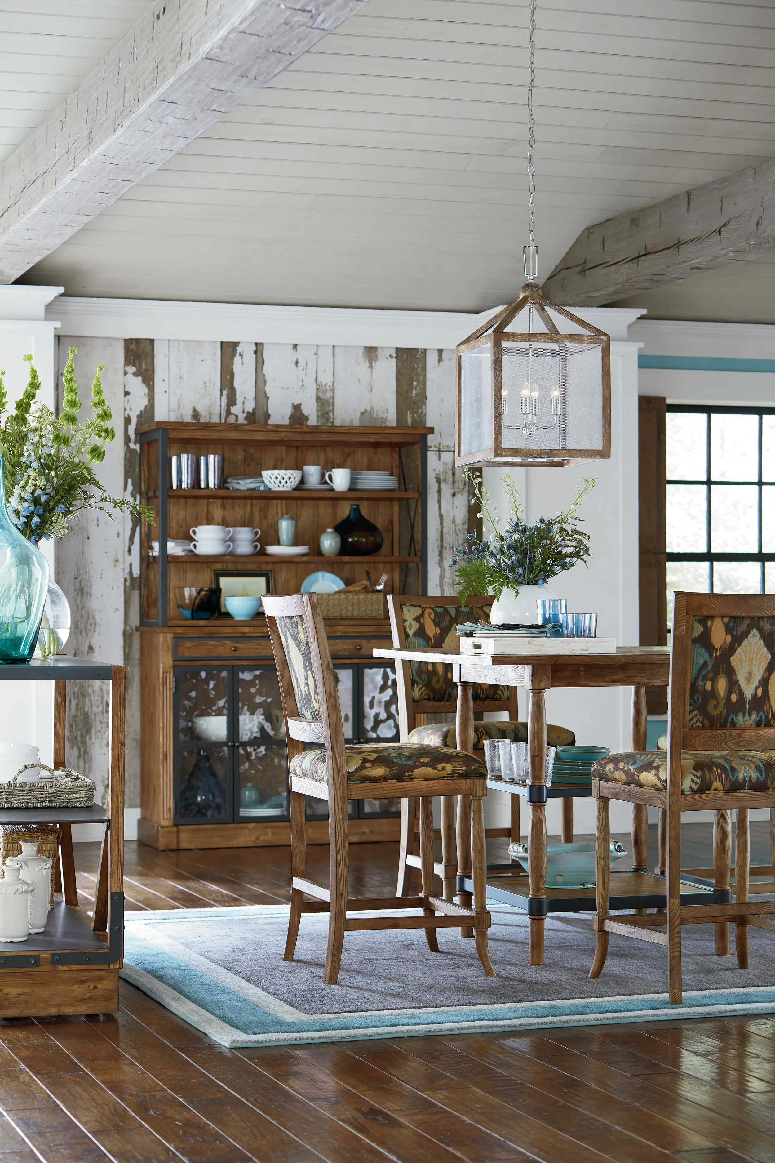 Rustic dining room ink illustration with wood table, patterned stools and a wooden hutch, rendered in warm neutral tones